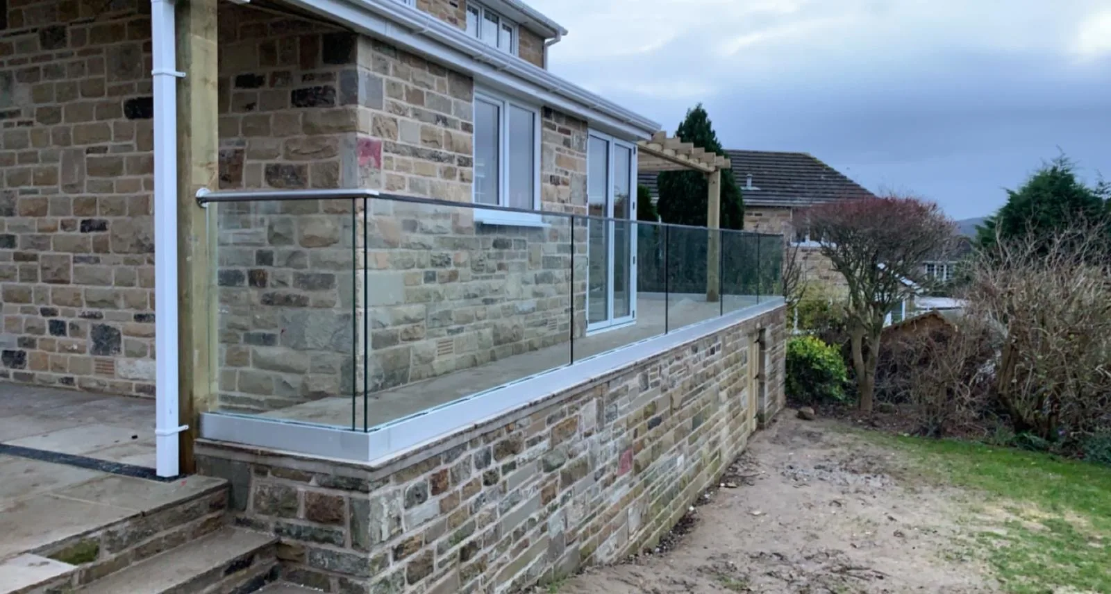 Glass balustrade with an aluminium base channel and handrail along a raised stone terrace